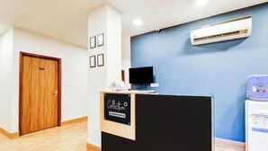 A reception area with a wooden door, a reception desk, a flat-screen TV, and an air conditioning unit. - Collection O GNRC Hospital Dispur (Guwahati)