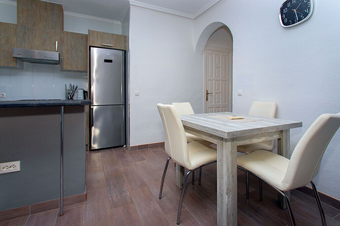 A modern kitchen with a stainless steel refrigerator, a wooden cabinet, and a dining table with four chairs.