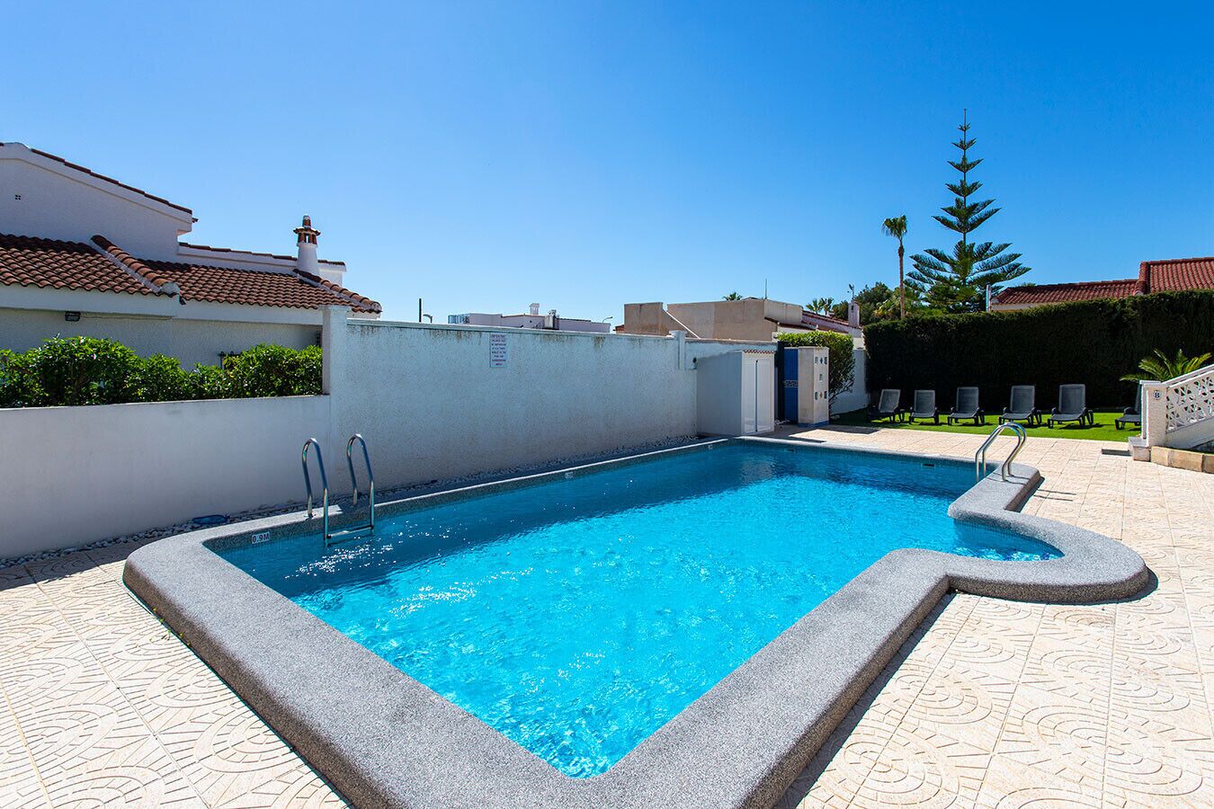 Piscina rectangular con agua azul cristalina, rodeada de un solado de baldosas y un muro blanco bajo.