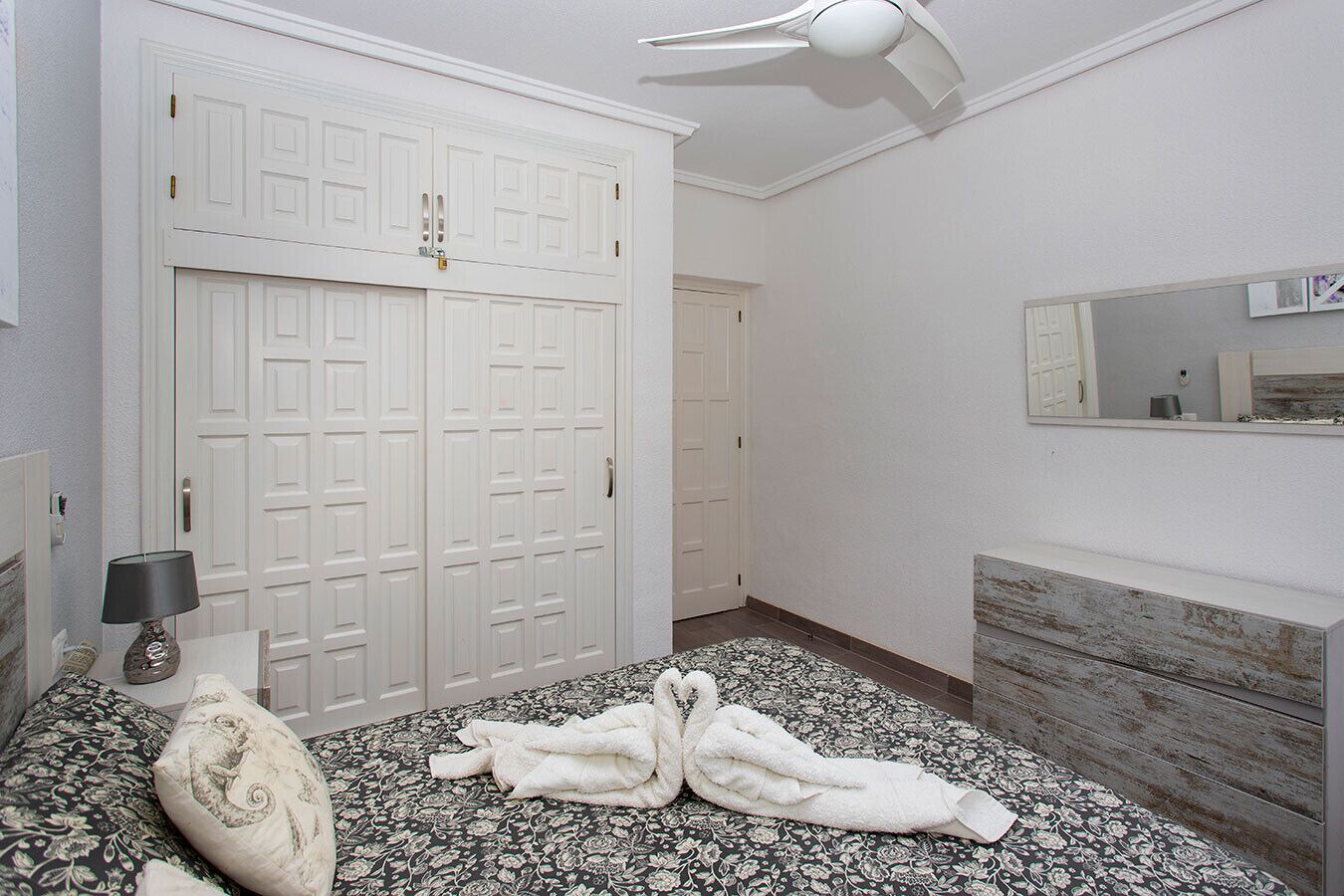 Ein Schlafzimmer mit einem Bett, einem Kleiderschrank, einem Spiegel und einem Deckenventilator.