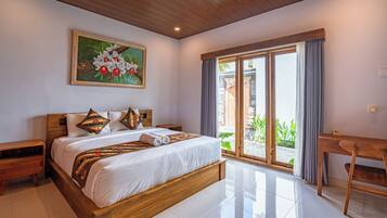 Un dormitorio bien iluminado con una cama grande, cabecera de madera, un cuadro, un escritorio y vistas a través de un ventanal.