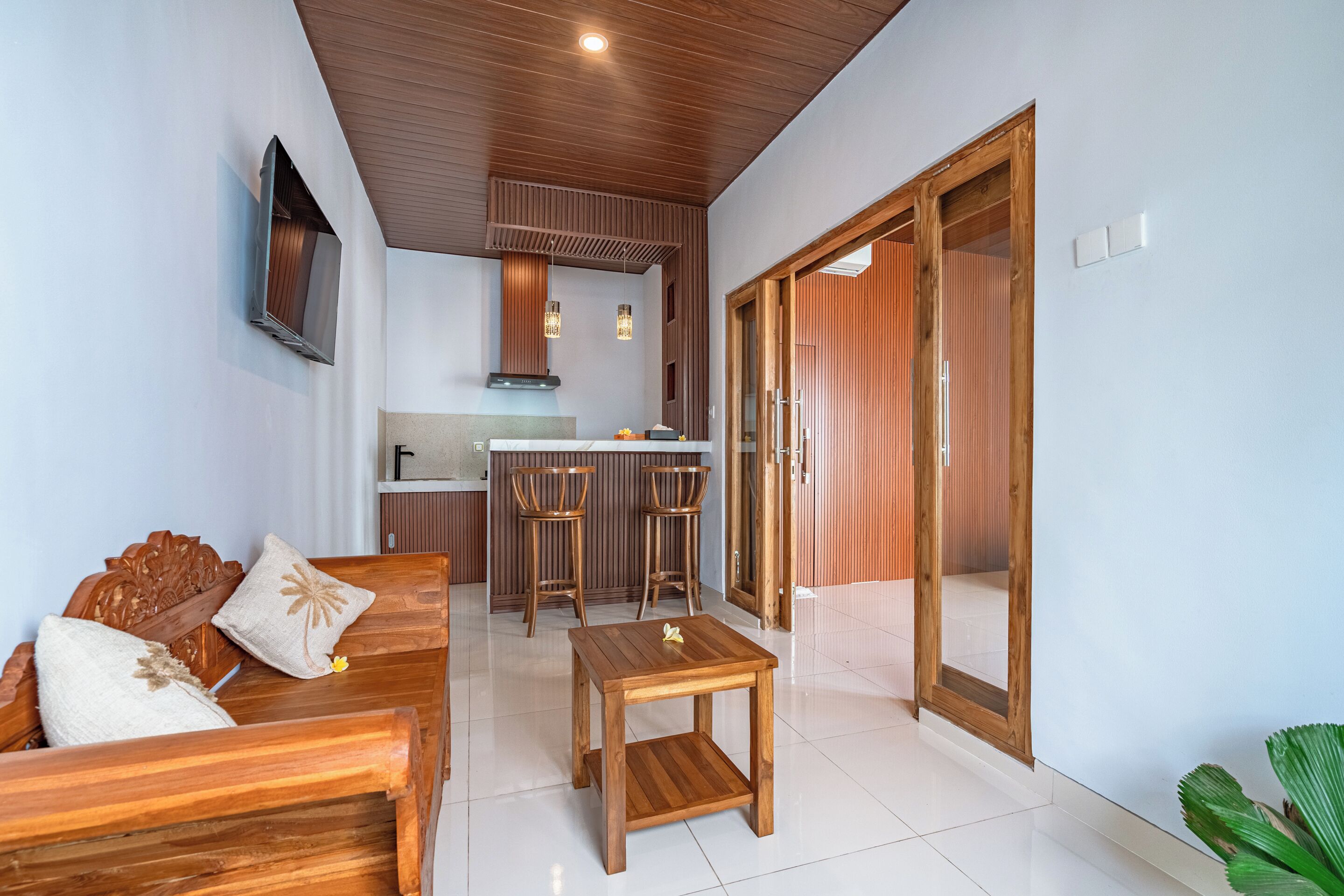 A modern living room with a wooden sofa, a coffee table, and a kitchen area with a bar and stools.