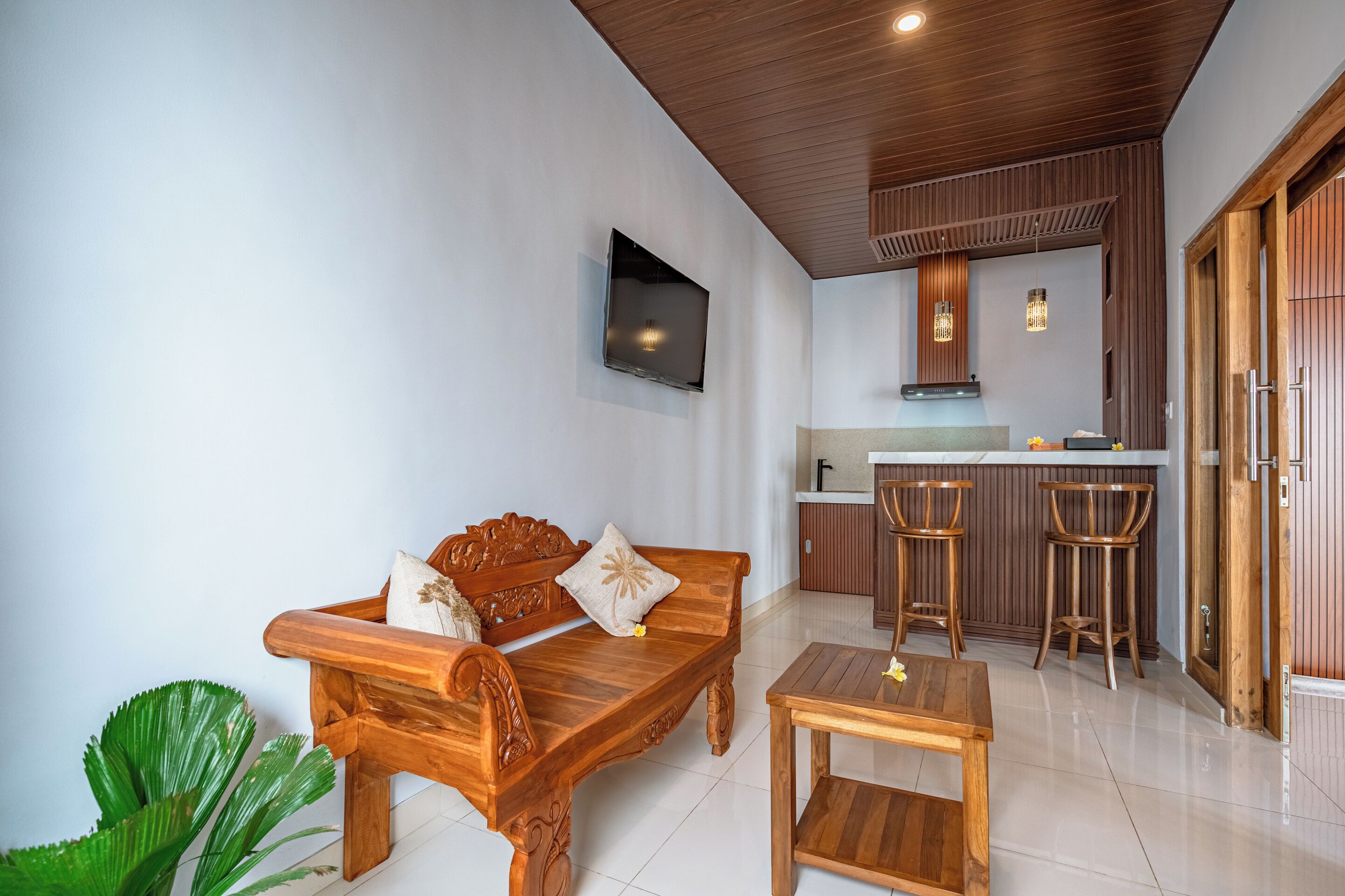 A modern living area with a wooden sofa, a small table, and a kitchen with a bar counter.