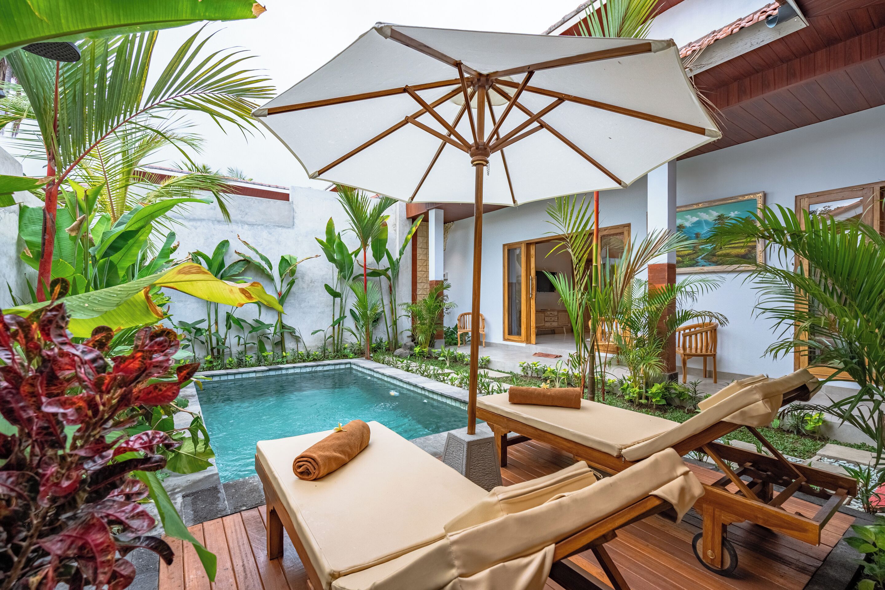 Un área junto a la piscina con sillones de descanso, una terraza de madera y una sombrilla grande.