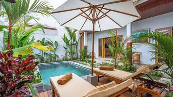 Un área junto a la piscina con sillones de descanso, una terraza de madera y una sombrilla grande.