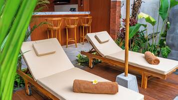 A wooden deck with two lounge chairs, a small bar area, and tropical plants.