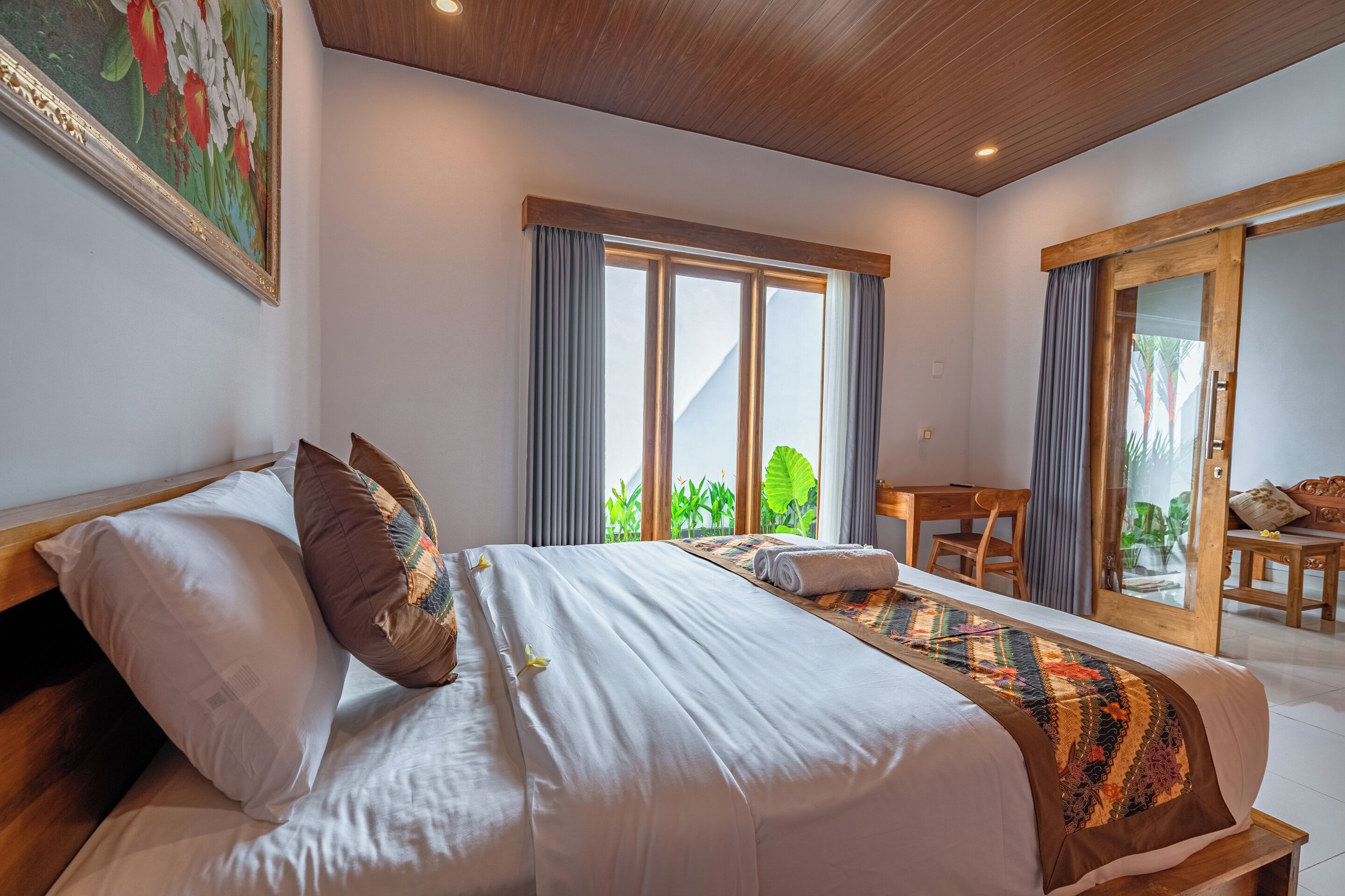 Un dormitorio con una cama grande, un escritorio y vistas al verdor exterior.