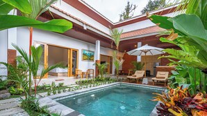 Ein Poolbereich mit gefliestem Deck, Liegestühlen und einer Holzpergola.