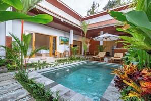 Un área de piscina con deck de baldosas, sillas de descanso y una pérgola de madera.