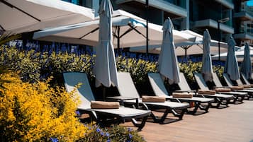 Een rij ligbedden met witte parasols, gerangschikt op een houten terras, met gele en blauwe bloemen op de achtergrond.