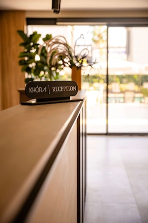 A reception desk with a sign reading 'KHOIRA | RECEPTION' and a potted plant in the background.