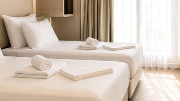 Een hotelkamer met twee bedden, een kledingkast en een groot raam met gordijnen.