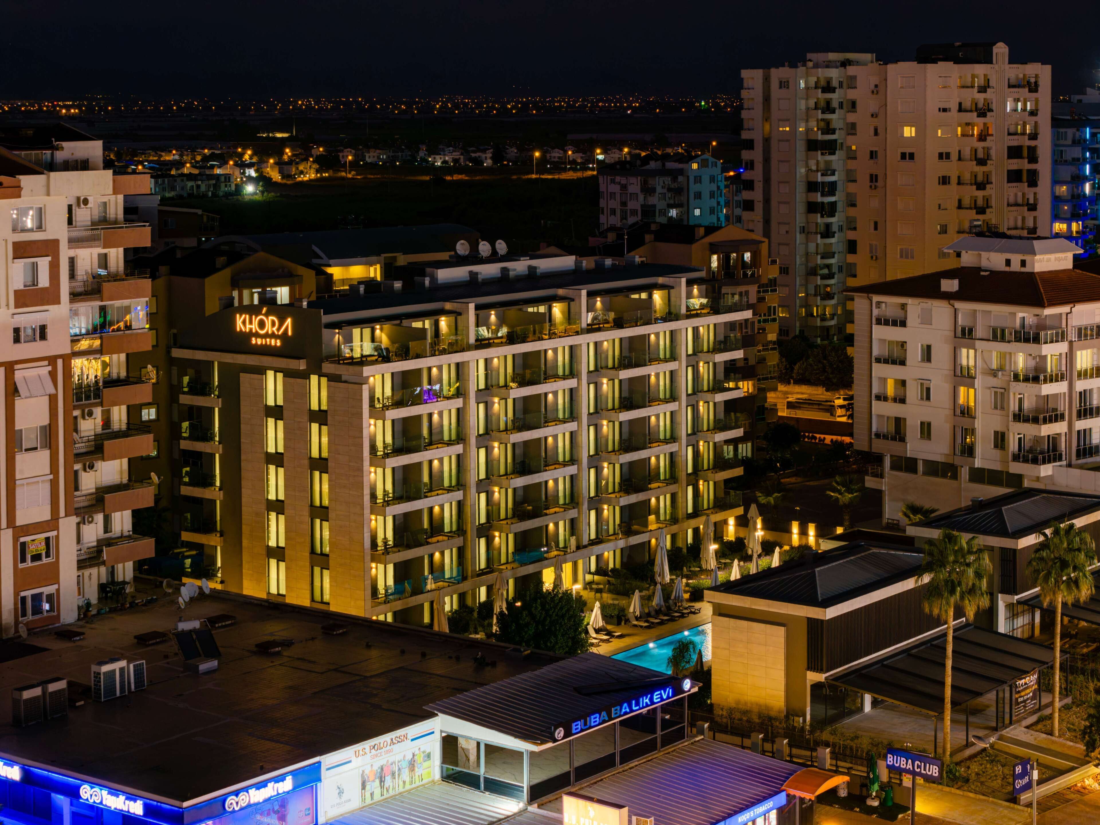 A multi-story hotel with a rooftop pool area, signage for 'KHOPIA SUITES' and 'BUBA BALIKEVI,' and a 'BUBA CLUB' sign.