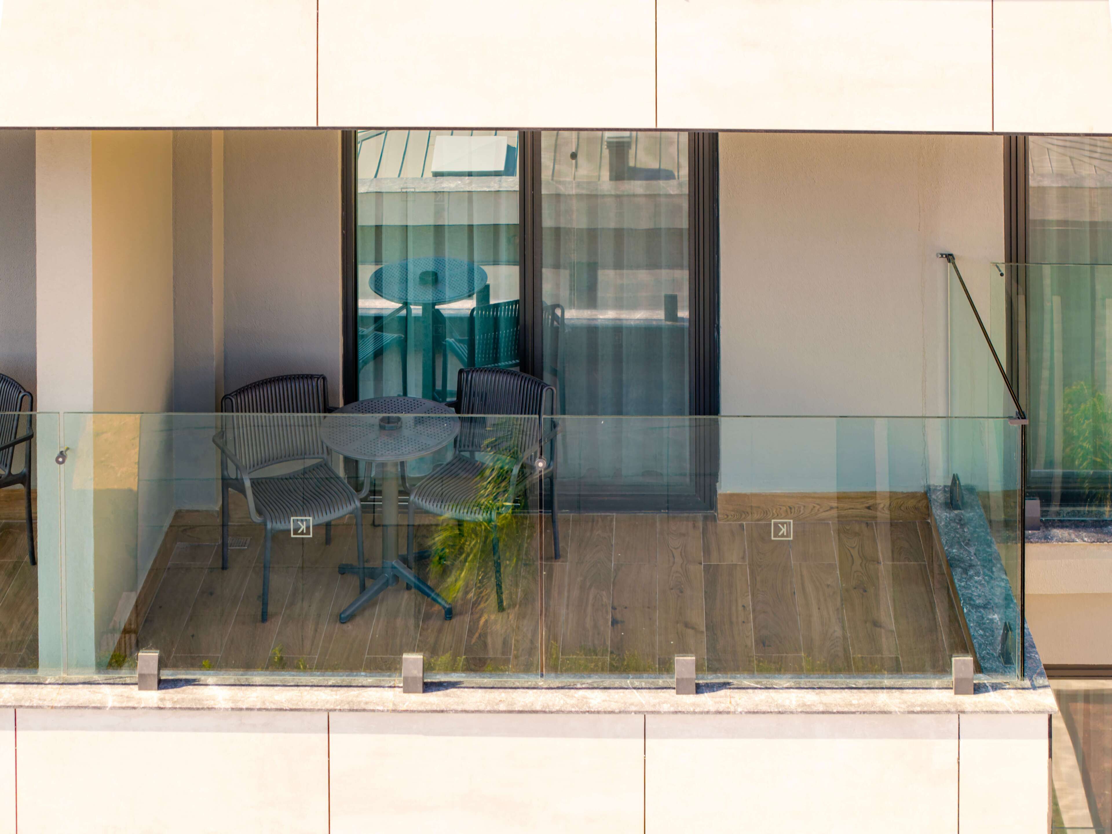 Een moderne zithoek buiten, met een glazen balustrade, een ronde tafel en vier stoelen.