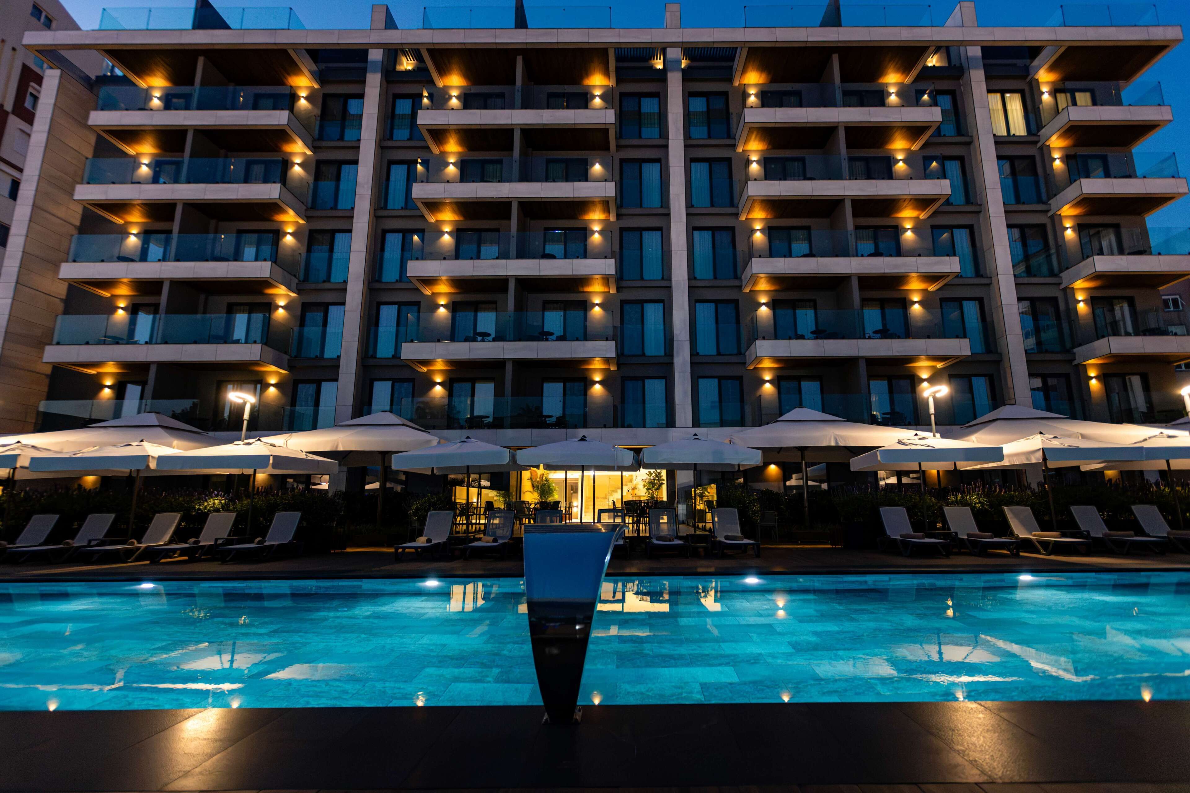 A hotel with a swimming pool, multiple balconies, and outdoor seating with umbrellas.