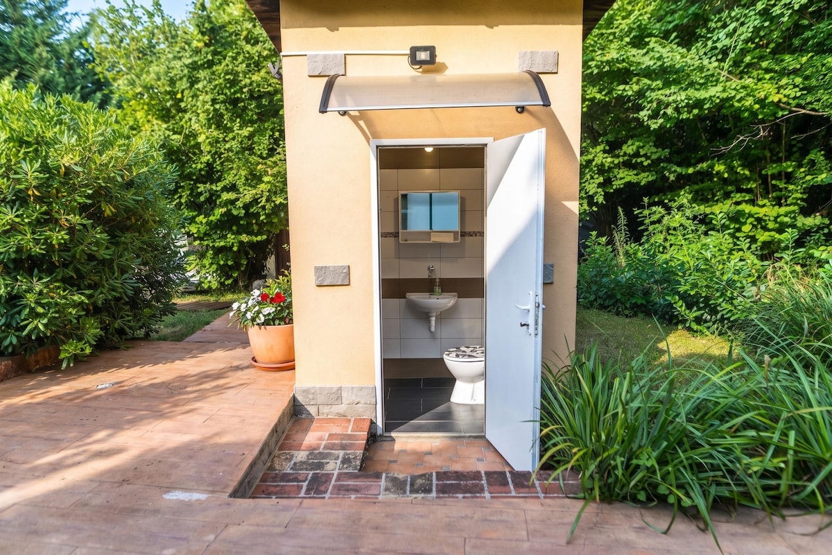 A private outdoor bathroom with a toilet, sink, and shower area, surrounded by lush greenery.