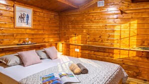 A wooden cabin room with a bed, pillows, a book, and a framed picture on the wall. - Paradise Forest Glamping Rooms (Koper)