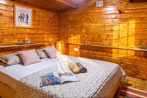 Quarto de cabana de madeira com uma cama, travesseiros, um livro e um quadro na parede.