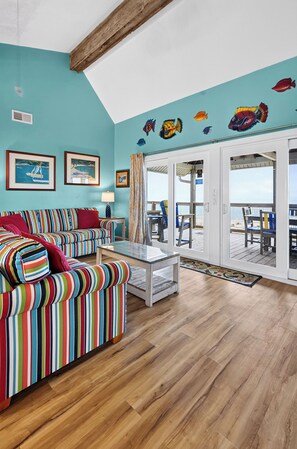 Um quarto com um sofá listrado, uma mesa de centro de vidro e vista para o mar através de uma porta de vidro.