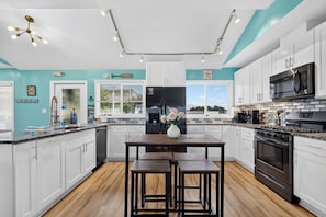 A modern kitchen with white cabinets, a black refrigerator, a stainless steel oven, and a dining area with a table and benches. - Sea Ya! Beach Front! Pet Friendly! Hot Tub! (St. George Island)