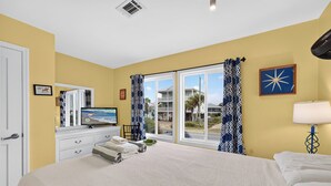 Ein Hotelzimmer mit einem großen Bett, einem Fernseher, einer Kommode und Blick auf den Strand durch die Fenster.