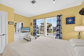 A hotel room with a large bed, a television, a dresser, and a view of the beach through the windows. - Sea Ya! Beach Front! Pet Friendly! Hot Tub! (St. George Island)