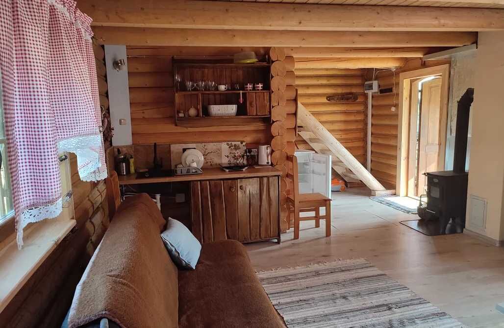 Interior acollidor d'una cabana amb una cadira de fusta, una cuina amb una estufa i una escala que condueix a un nivell superior.