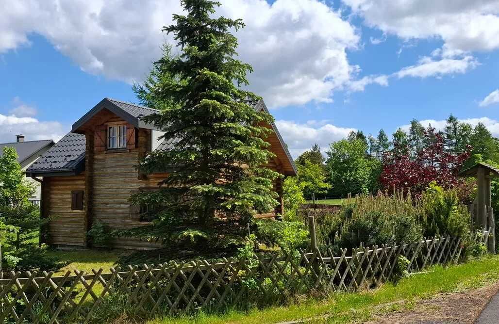 Una cabana de fusta amb teulada inclinada, envoltada per una tanca de fusta i vegetació abundant.