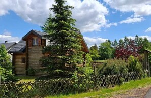 Une cabane en bois, dotée d’un toit à pente, entourée d’une clôture en bois et d’une végétation luxuriante.