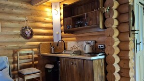 Interior acollidor d'una cabana amb elements de fusta, una cuina amb electrodomèstics bàsics, taula de menjador amb cadires i una petita zona de seients.