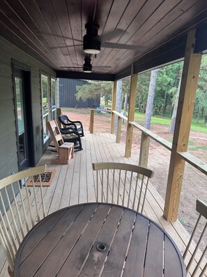 A covered outdoor deck with a table and chairs, wooden railings, and a view of the surrounding area. - New Pondside Retreat Near Lake Ouachita (Royal)