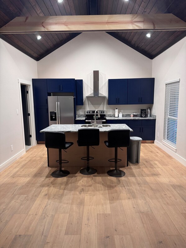 A modern kitchen with a central island, dark blue cabinets, a stainless steel refrigerator, and a gas stove.