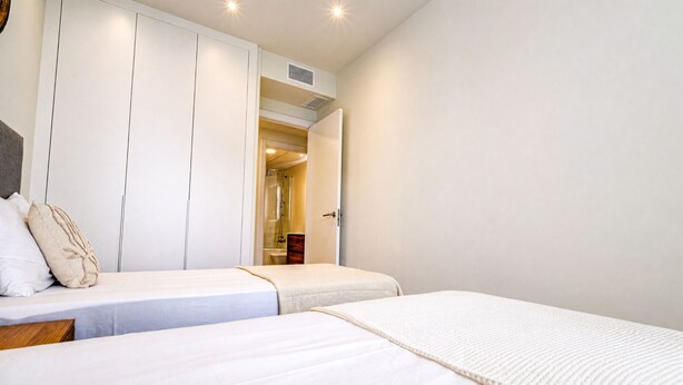 A hotel room with two beds, a wardrobe, and a bathroom visible through an open door. - Unic Serenity Apartment Javea (Javea)