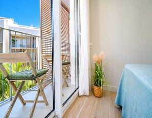 Ein Balkon mit Holzstuhl, einem kleinen Tisch, einem Topfpflanze und einer blauen Tischdecke.