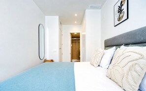 A modern bedroom with a bed, a bedside table, a mirror, and a door leading to a bathroom. - Unic Serenity Apartment Javea (Javea)