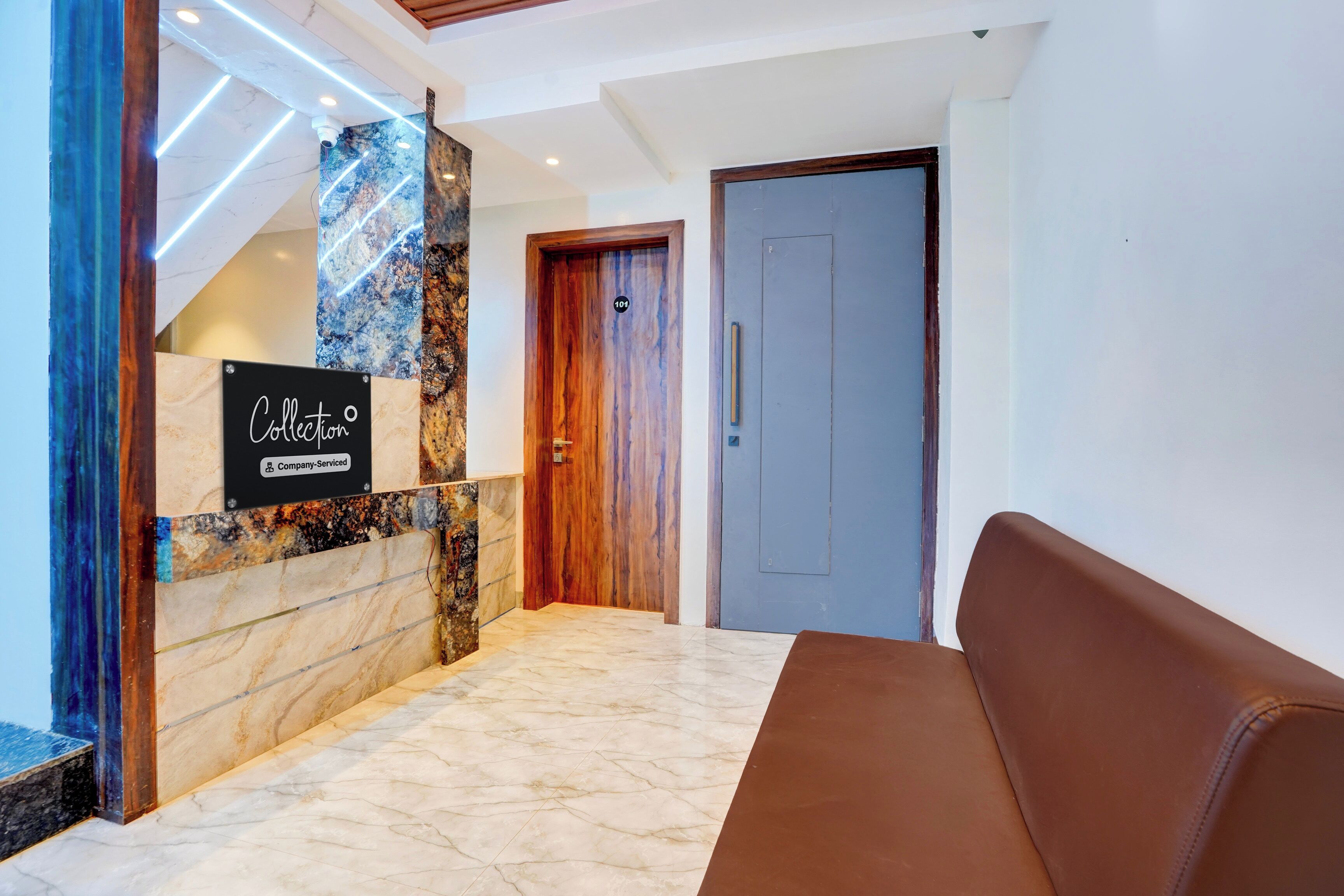 Un vestíbulo de hotel con una recepción, una pared de mármol y un sofá de cuero marrón.