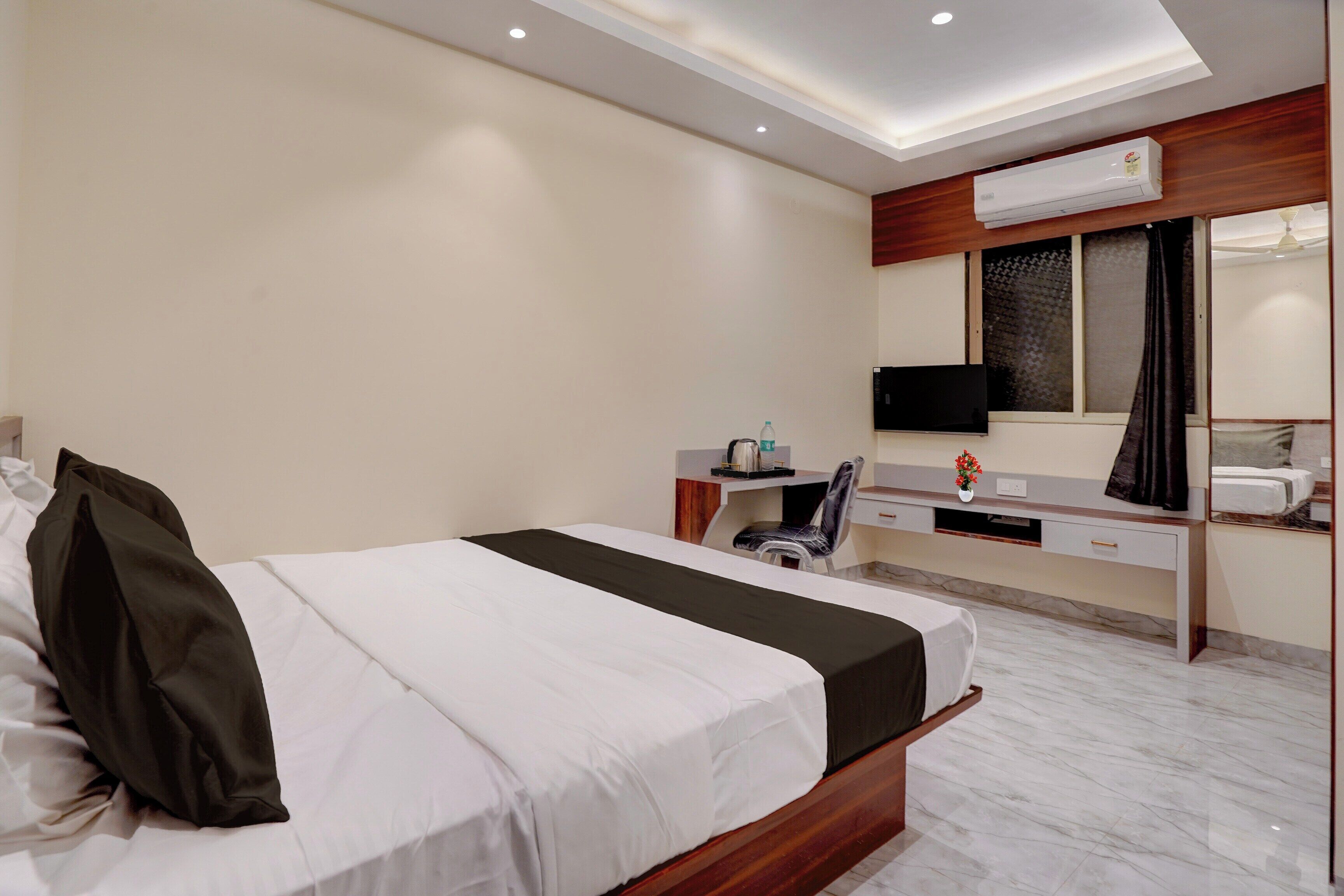 A hotel room with a bed, a desk, a chair, a TV, and an air conditioning unit.