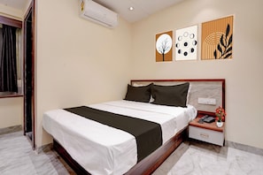 A hotel room with a bed, bedside table, and a wall-mounted air conditioner.