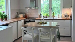 Een moderne keuken met witte kasten, een centraal kookeiland met stoelen, een ingebouwde oven en een raam met uitzicht op groen.