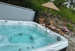 A hot tub with a wooden deck and chairs, surrounded by greenery.