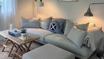 A modern living room with a grey sofa, a wooden coffee table, and a grey ottoman.