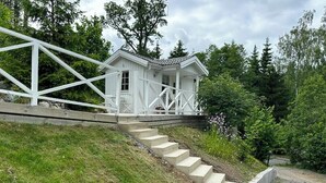 Een witte houten chalet met een veranda, omringd door een grashelling en bomen.