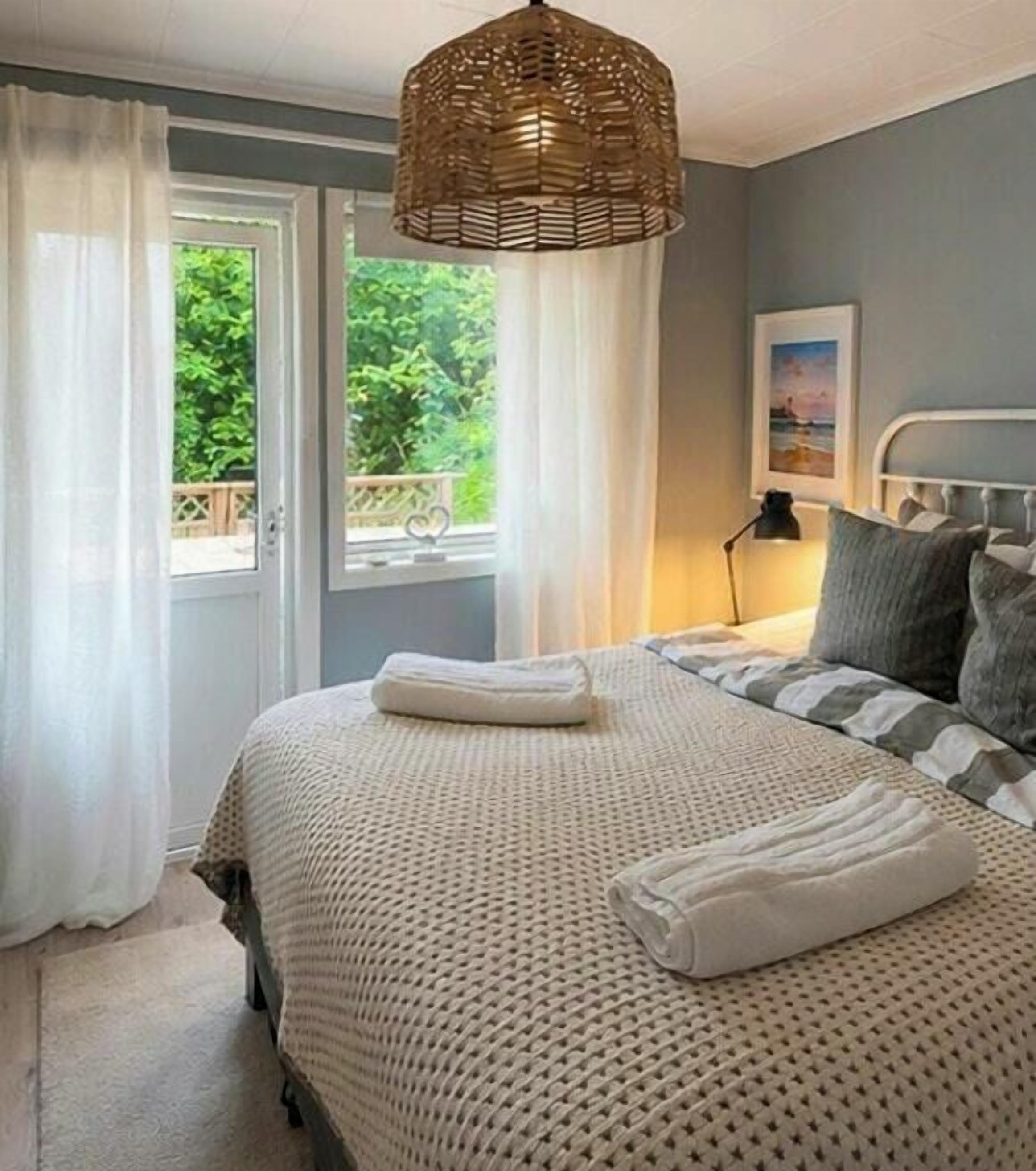 A bedroom with a bed, a bedside lamp, a window with curtains, and a view of greenery outside.