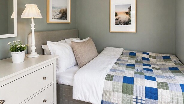 Een slaapkamer met een bed, een nachtkastje met een lamp, een dressoir en twee ingelijste foto's aan de muur.