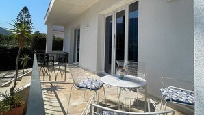 Eine überdachte Terrasse im Freien mit Tisch und Stühlen, einem Blumentopf und Blick auf die Umgebung.