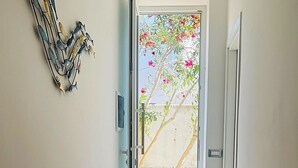 Ein Flur mit einer Tür, die auf einen Balkon mit Blick auf einen Garten und einen Baum führt.