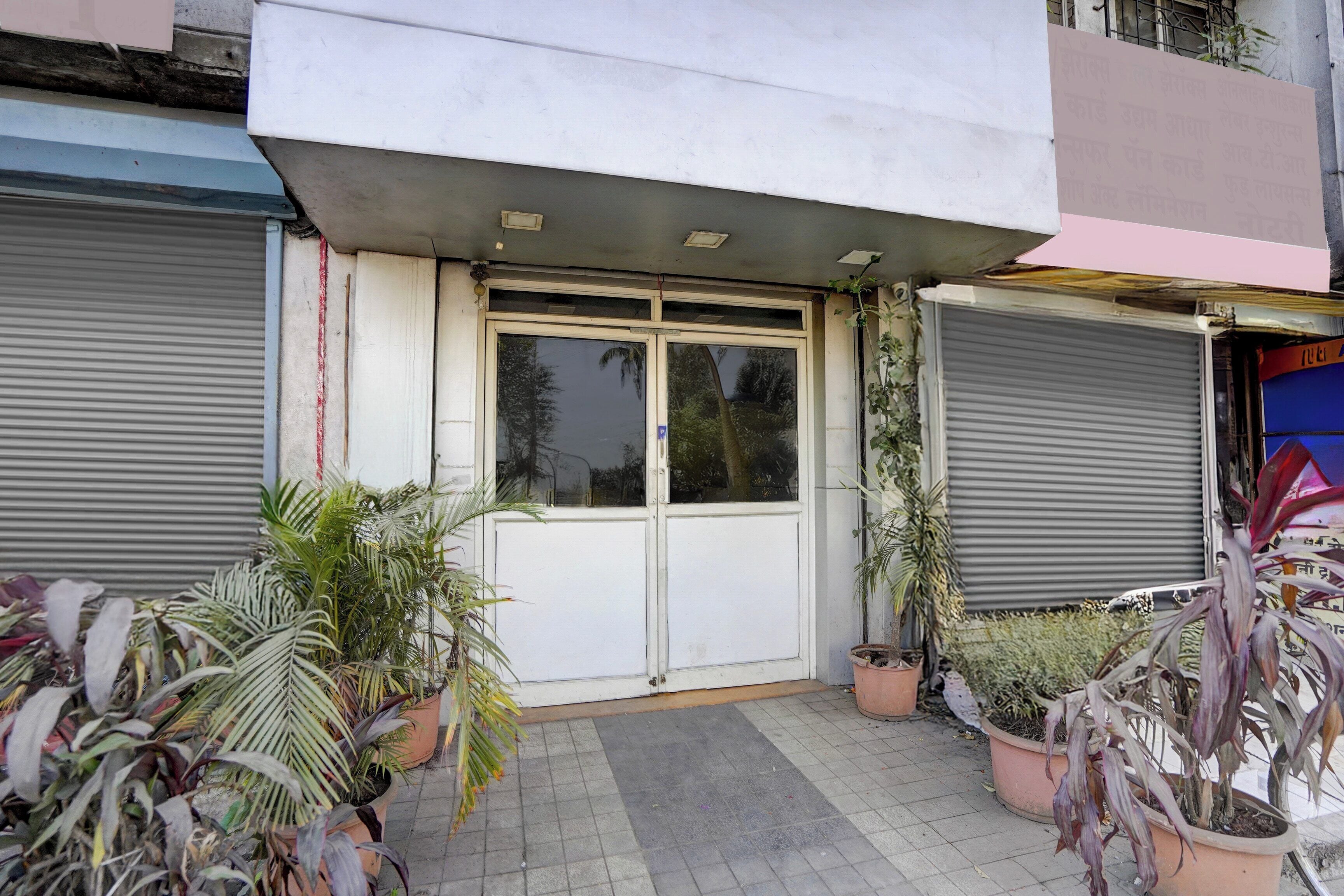 Una entrada de edificio con puerta cerrada, plantas en macetas y pavimento de baldosas.