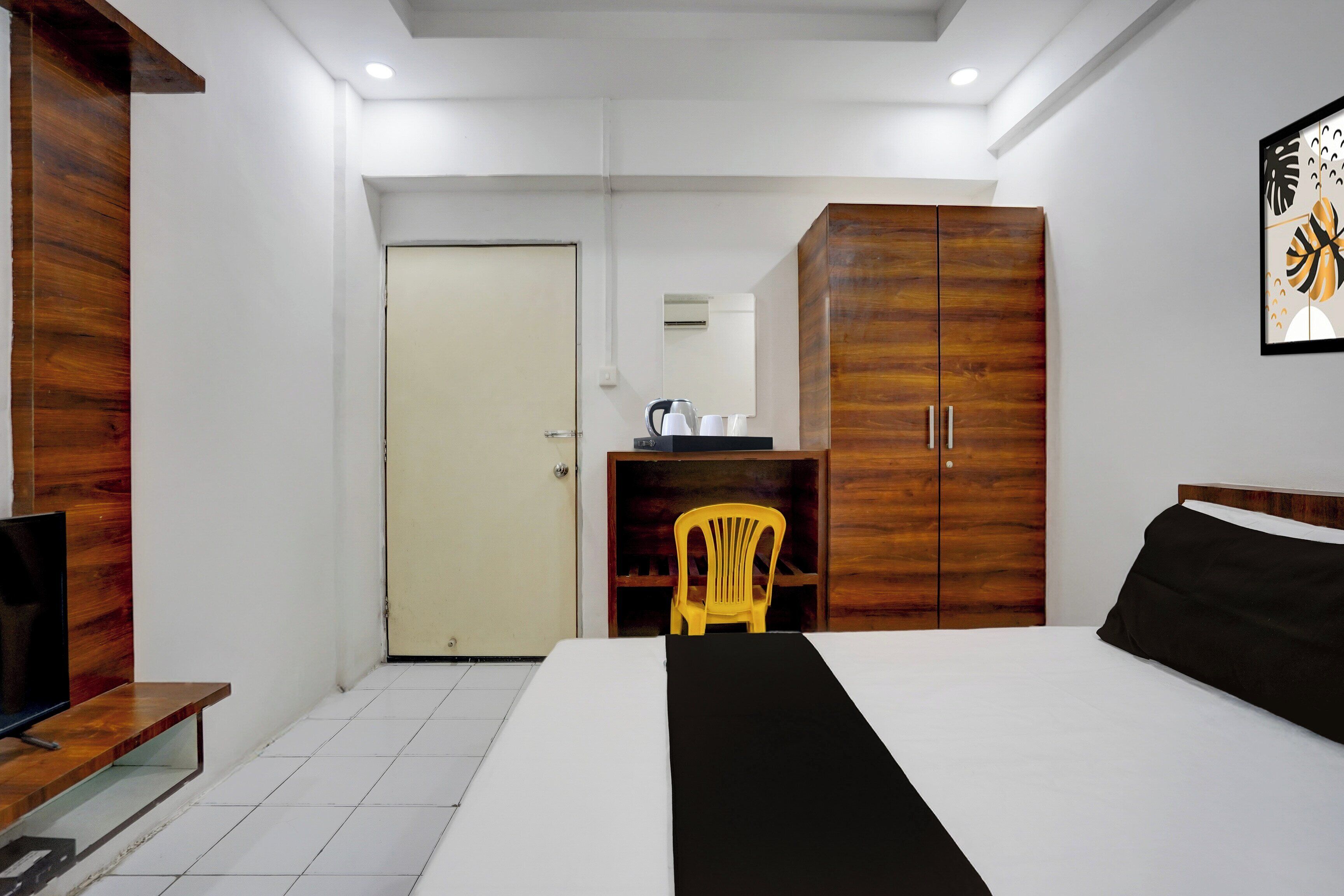 A hotel room with a bed, a wooden wardrobe, a desk with a chair, and a television.