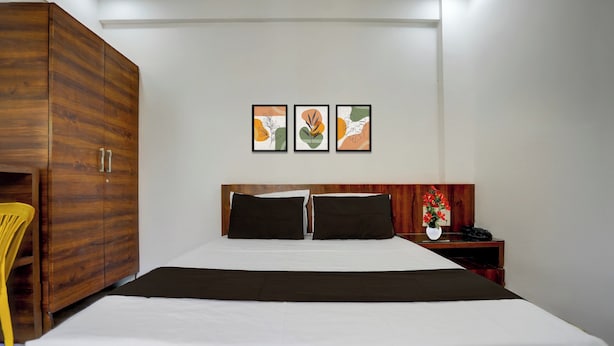 Una habitación de hotel con una cama grande, un armario de madera, una mesita de noche con un teléfono y un jarrón de flores, y tres cuadros en la pared.