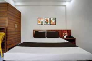 Une chambre d’hôtel avec un grand lit, une armoire en bois, une table de chevet avec un téléphone et un vase de fleurs, et trois œuvres d’art encadrées accrochées au mur.